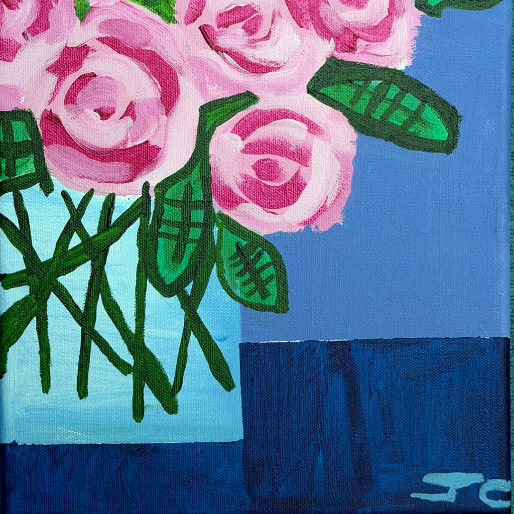 Large pink blooms with green leaves in clear vase on blue table